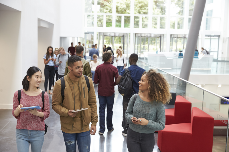 Students holding tablets and phone talk in university lobby